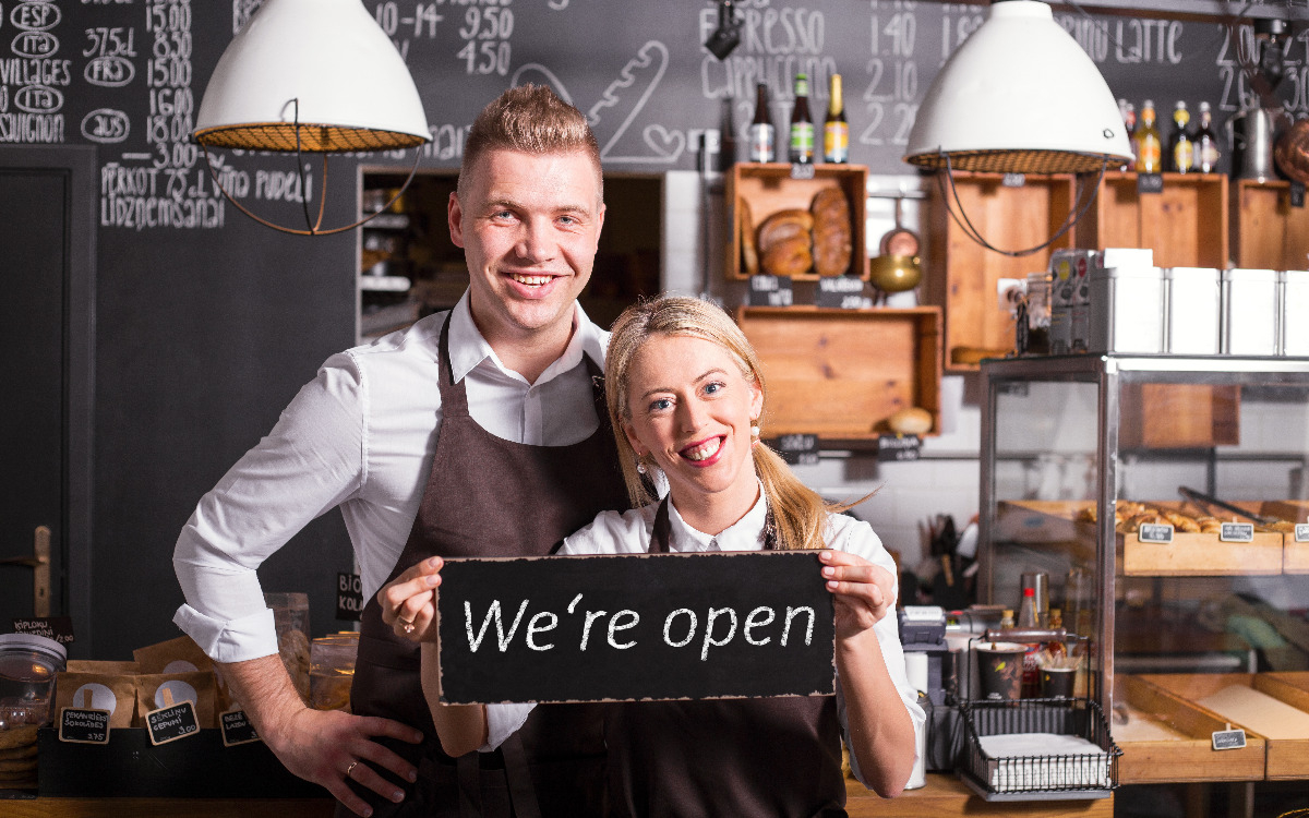 Two small business owners holding a "we're open" sign.