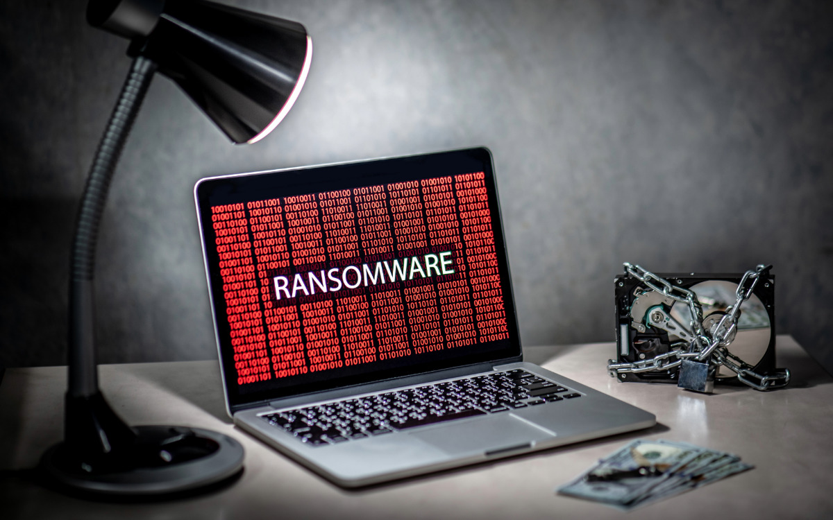 A laptop with the word Ransomware next to cash and a locked hard drive.