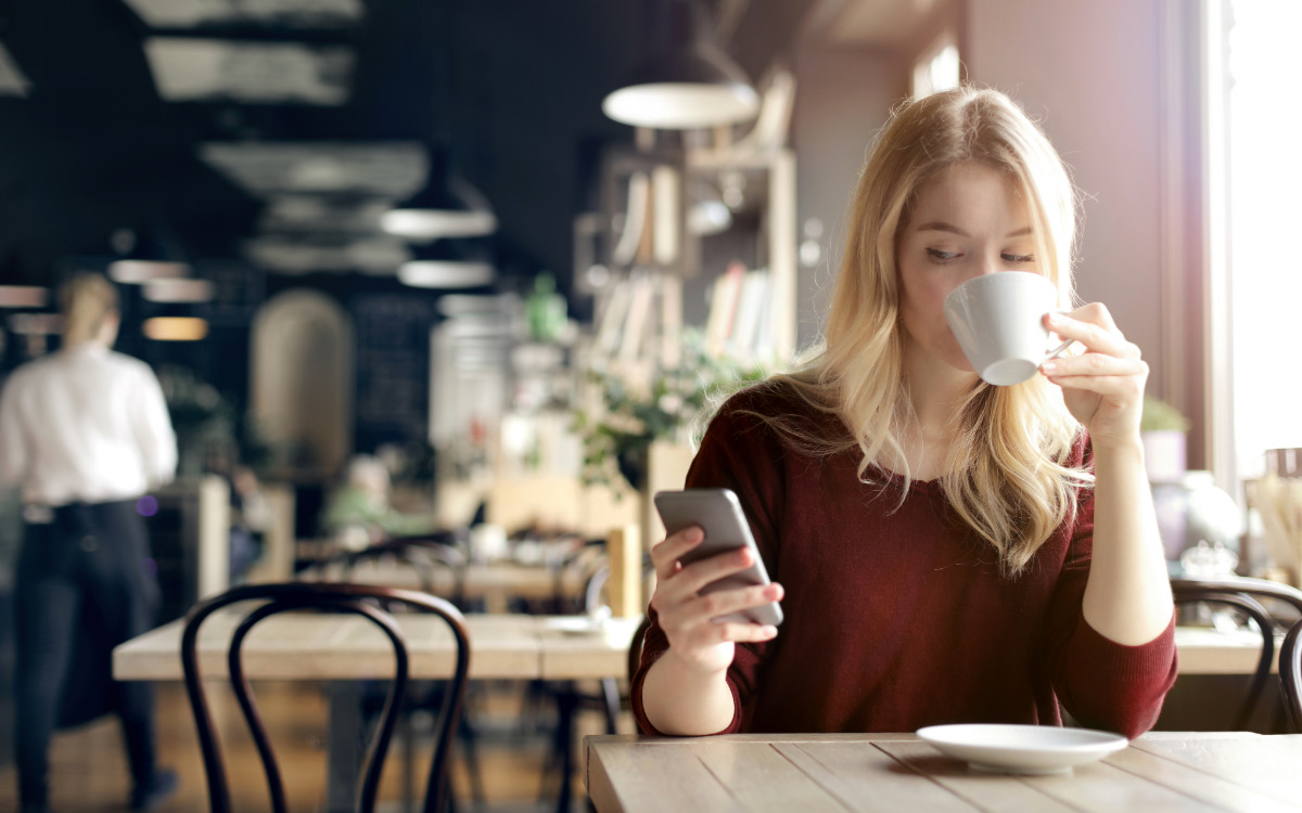 Woman drinking coffee and holding a phone while connected to public Wi-Fi.